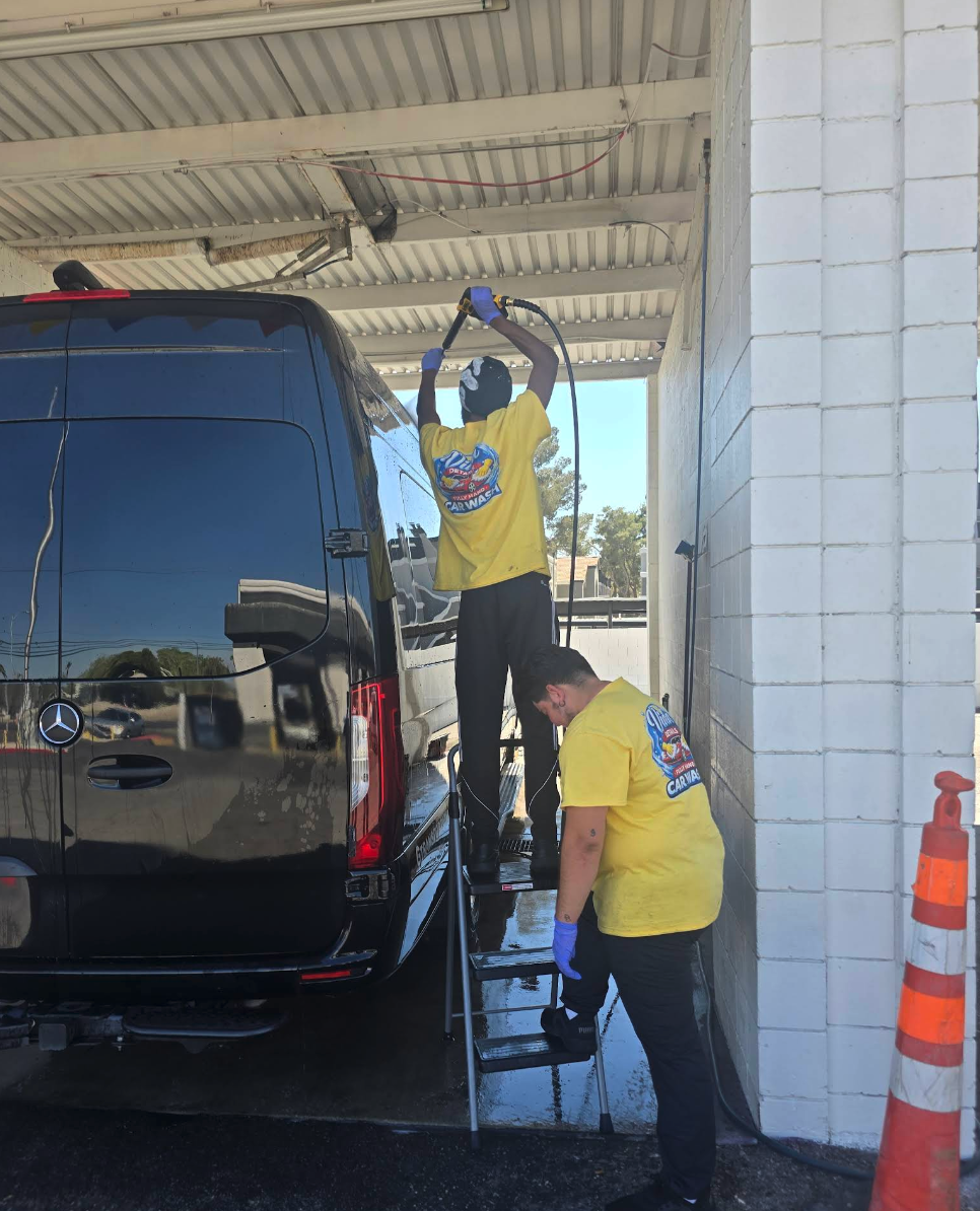 Two Vida Detail technicians in yellow shirts hand‑washing a black Mercedes Sprinter van in the wash bay.